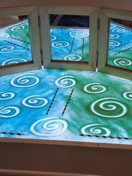A light table with colored sand and mirrors creates a mesmerizing invitation to explore patterns and symmetry. As children draw swirls in the sand, they can see their creations reflected and multiplied, adding a layer of magic to their mark-making.