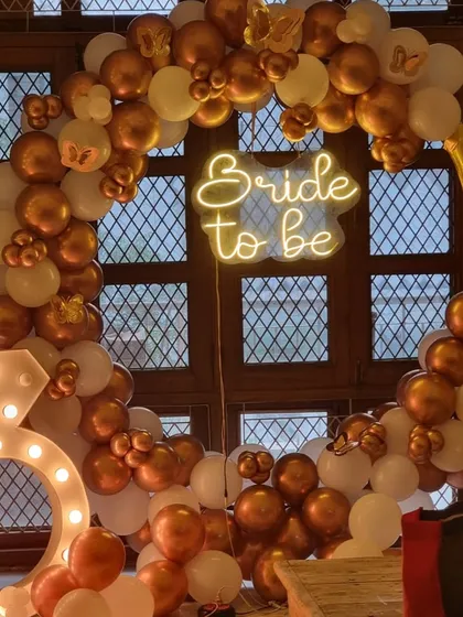 Another angle of the gold and white bachelorette party decor, highlighting the "Bride to be" neon sign and the full balloon arch.