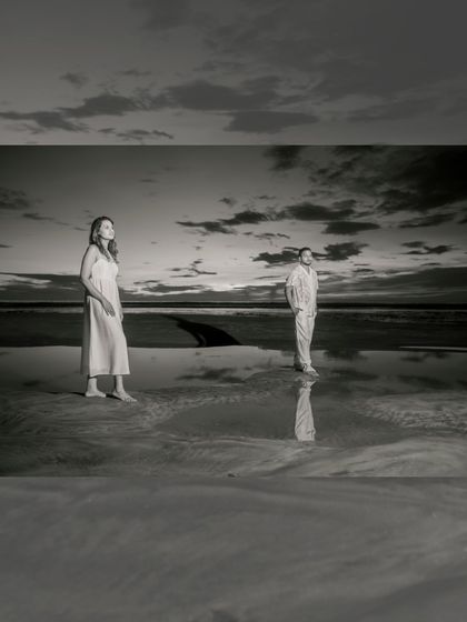 A dramatic black and white shot as dusk settles on the beach. The reflections in the wet sand and the moody sky create a powerful, artistic image.