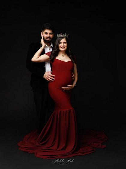 A regal couple's portrait. The deep red gown and crown paired with a classic suit against a dark background creates a look of timeless elegance and power.