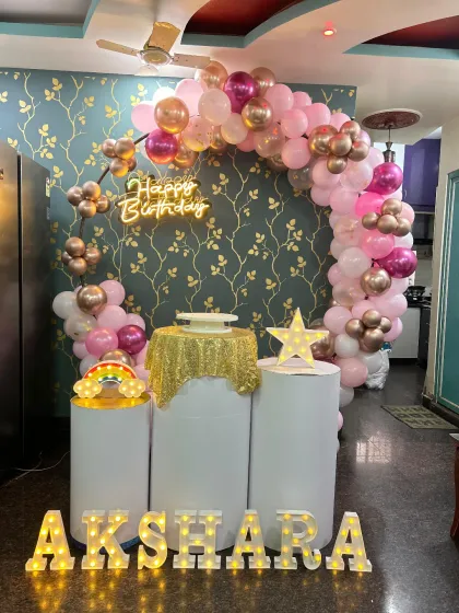 A lovely rose gold and pink balloon arch against a beautiful wallpapered background. This setup is perfect for an elegant at-home birthday celebration, complete with a neon sign and marquee letters.
