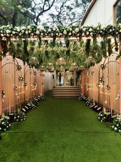 A beautiful pastel entrance for a wedding day. The walkway is lined with soft pink drapes and features a custom neon hashtag, making it a personalized and welcoming sight.
