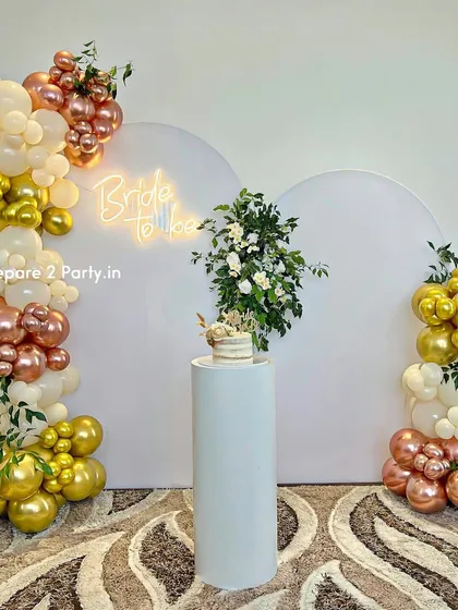 For a modern and chic bridal shower, we offer this elegant setup. It features clean white arched backdrops, a stylish "Bride to be" neon sign, and sophisticated balloon columns in cream, gold, and rose gold, accented with fresh greenery.