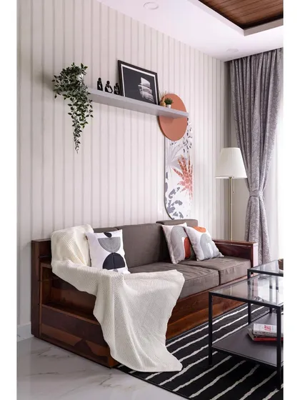 This living area showcases a blend of textures and patterns. The striped wallpaper provides a neutral backdrop for the solid wood sofa, while abstract art and geometric cushions add a contemporary, artistic touch.