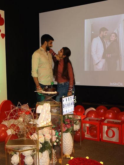 The cake cutting moment is always a highlight. Here, a couple shares a sweet moment during a birthday celebration, with their personal photos displayed on the screen in the background.