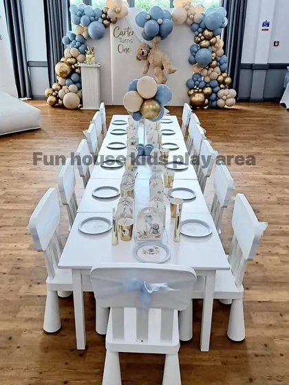 A close-up view of our elegant white table and chair setup for a "Teddy Bear" themed first birthday. The chairs are decorated with delicate blue sashes, showing how easily our classic furniture can be customized.
