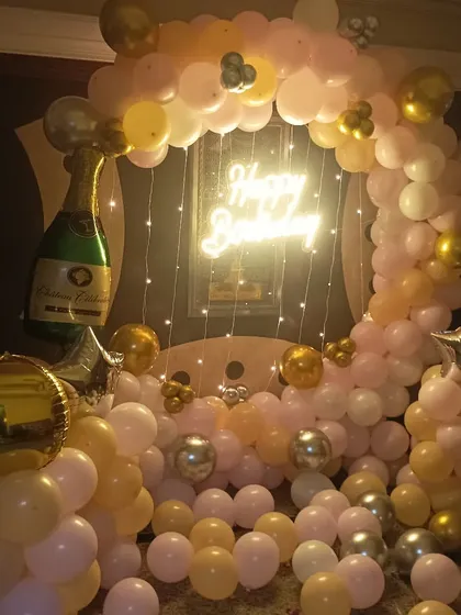 A beautiful ring decoration with pastel and gold balloons, a champagne foil balloon, and a neon sign.