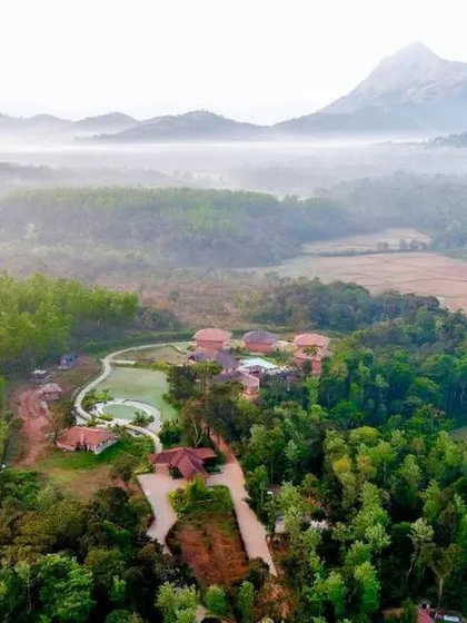 A misty morning at a resort in Sakleshpur, with the property nestled in a valley surrounded by lush forests and mountains.