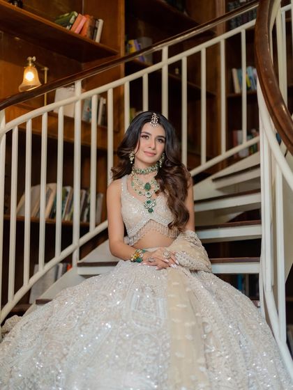 An ivory lehenga offers a canvas for modern elegance. Paired with statement emerald jewelry, this look is both graceful and striking, captured here on a beautiful spiral staircase.