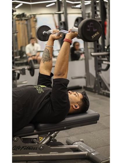 A member performs a close-grip bench press with an EZ curl bar, an effective exercise for targeting the triceps and inner chest.
