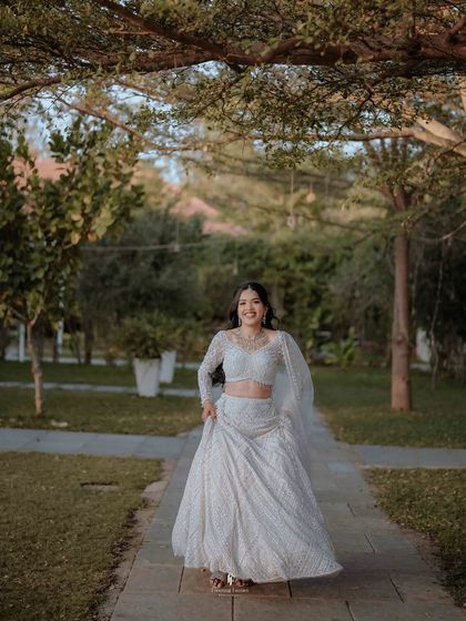 A joyful, candid shot of the bride in her white reception lehenga, walking through a garden.