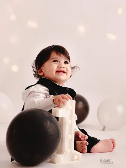 A candid moment of pure happiness during a first birthday session. We use a clean, minimalist setup with black and white balloons to keep the focus on your child's expressions.
