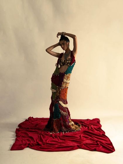 A wide shot showing the full scale and drama of the colorful, textured gown against a red floor, creating a powerful visual statement.
