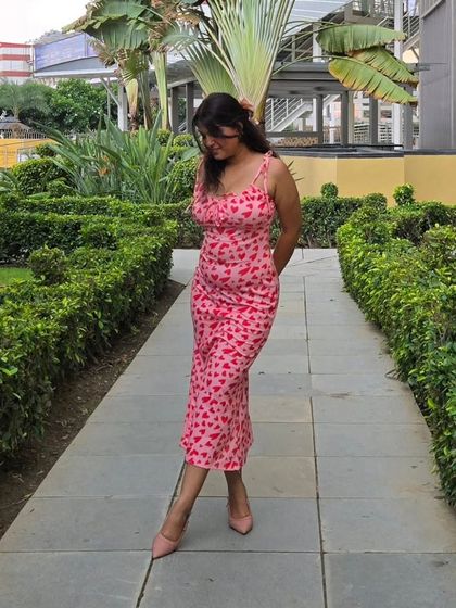 A walking shot in the pink heart-print dress, paired with matching pink pointed-toe heels. A monochrome shoe pairing elongates the legs and creates a cohesive, polished outfit.