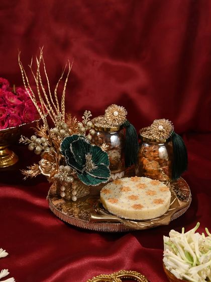 A luxurious Teej hamper with a malai ghewar, ornate jars for treats, and stunning gold and green floral decorations.