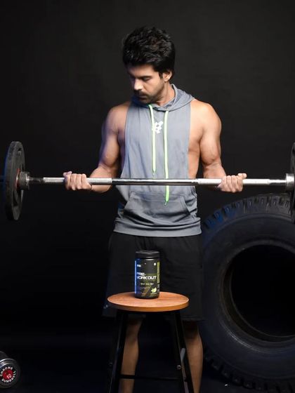 Here, the male model performs a bicep curl with a barbell, while the pre-workout supplement sits on a stool in front of him. This setup visually suggests the product is the fuel for the workout that is happening.