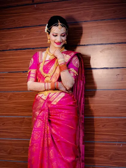A full-length portrait of a bride in a vibrant pink Kanjeevaram saree, showcasing the complete traditional bridal look.