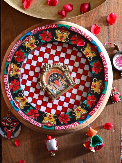 My hand-painted dedication to the fierce goddess Kaali, captured in a beautifully styled flat-lay. The artwork is set in a restored clock frame, with a checkerboard background and a border of hibiscus flowers and Kaali faces.