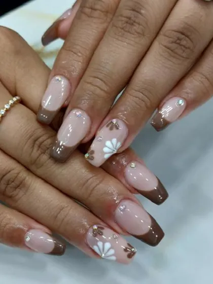 We love creating unique color combinations, like this chocolate brown French manicure. The design is elevated with hand-painted white floral details and tiny rhinestone accents.
