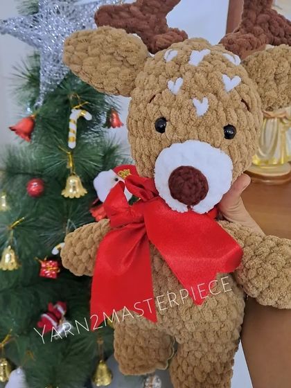 A plush reindeer toy, decorated for Christmas with a big red bow.