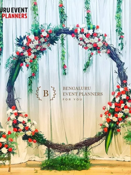 This rustic and elegant circular arch is made from natural twigs and adorned with clusters of red and white flowers. It serves as a beautiful and modern backdrop for an engagement ceremony, pre wedding event, or intimate reception.