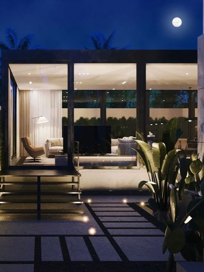 A night view of the same glass-encased patio lounge. The interior and exterior lighting creates a warm and inviting atmosphere, turning the garden into a usable space after dark.