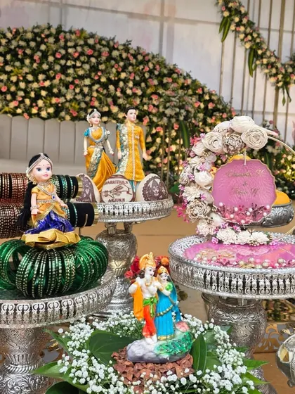 A display for a bangle ceremony, with dolls, stacks of bangles, and a floral ring platter.