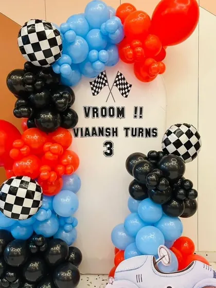 A "Vroom" racing car-themed decoration for a 3rd birthday, using red, blue, and black balloons with checkered flag details.