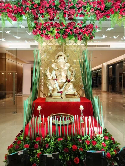 A Ganesha idol placed at the entrance for blessings. The setup is framed by a canopy of red flowers and accented with tall grasses and candles, blending tradition with modern design.
