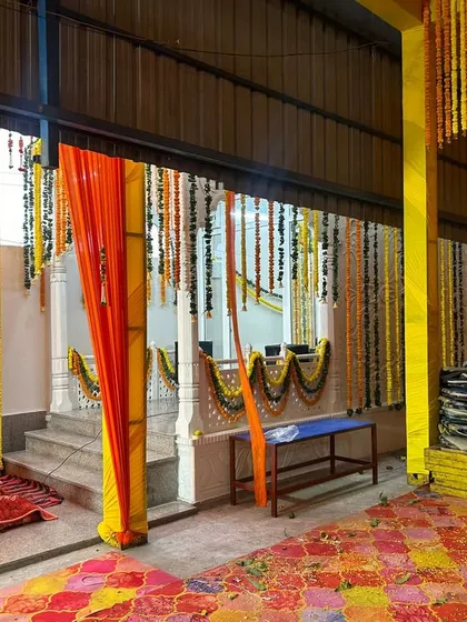 This image shows the inside of a tented area decorated for a wedding function. The combination of orange and yellow fabric with hanging flower strings creates a warm and traditional environment.