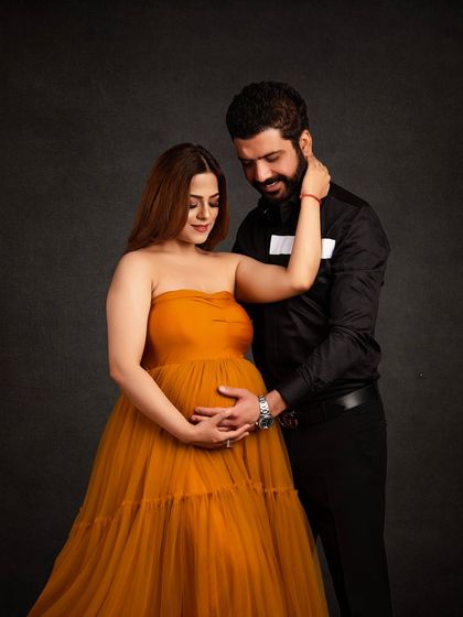 An intimate and classic couple portrait against a dark grey backdrop. The contrast between her mustard tulle gown and his black shirt creates a warm and sophisticated look.