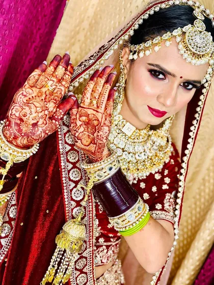 A stunning bride with her hands held up, showcasing the rich, dark stain of her wedding mehndi. The color is vibrant and eye-catching.