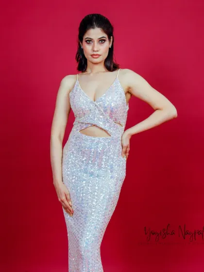 A full-body shot from the ad film, showcasing the complete look. The makeup complements the sparkling dress and bold red background.