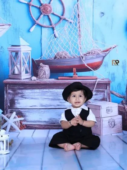 A baby boy sits among the props of a sailor-themed photoshoot. The detailed backdrop and props like lanterns and fishing nets create an authentic maritime atmosphere.