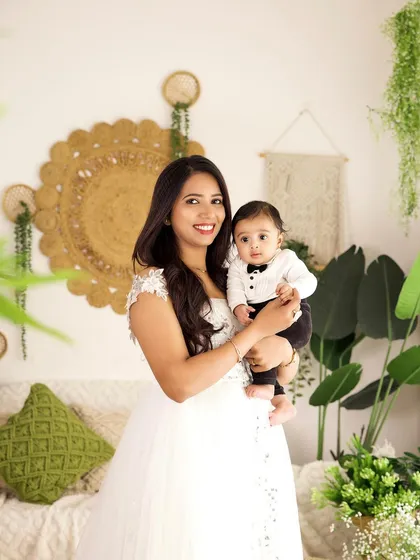 A proud mother holds her baby boy, who is dressed in a charming tuxedo-style outfit. This portrait showcases our boho studio's versatility.