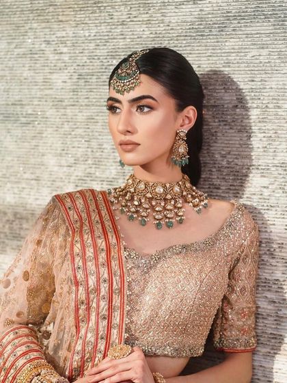 A classic and elegant bridal look. The makeup is warm and subtle, with a focus on a flawless base and softly defined eyes, perfectly complementing the gold and peach lehenga.
