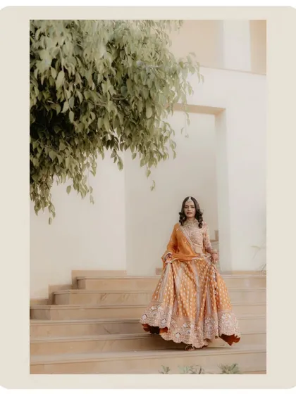 The bride descending the stairs, her lehenga in full view. The framing with the tree leaves adds a natural, soft touch to the portrait.