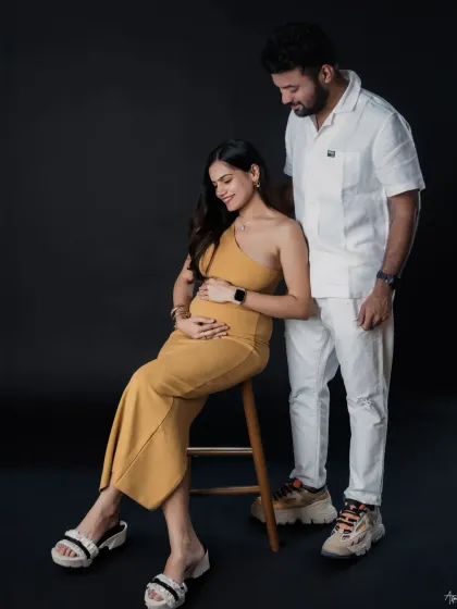A full-length portrait showing the couple's stylish and modern approach to their maternity shoot. The simple, dark backdrop allows their personalities and connection to shine.