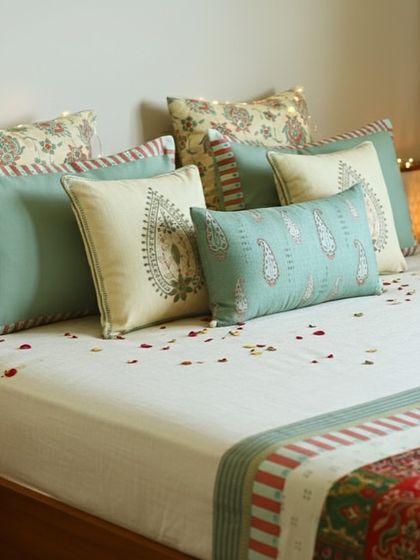 A festive bedding arrangement featuring our curated cushions. The mix of paisley prints, stripes, and solid colors in a soft sage green and cream palette creates a look that is celebratory yet serene.