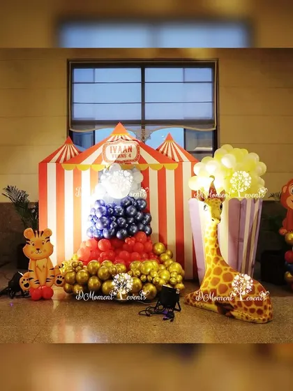 A cute carnival-themed corner decoration. The setup includes a popcorn box made of balloons, a circus tent prop, and cutouts of a giraffe, tiger, and monkey.
