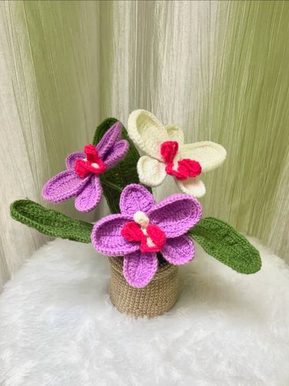 I also make exotic flowers like these crochet orchids. This arrangement features purple and white orchids with detailed centers, all nestled in a handmade pot.