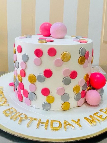 A fun and playful birthday cake decorated with colorful polka dots and spheres in pink, silver, and gold.