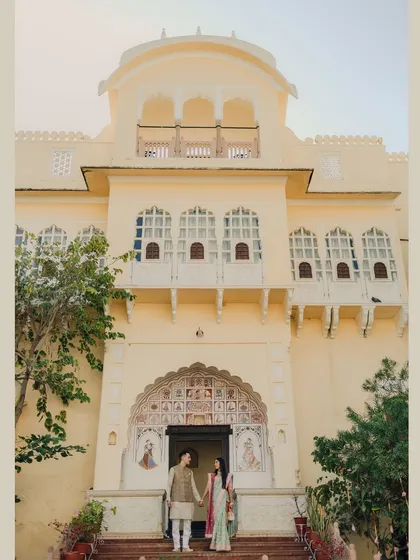 A full-length shot of the couple standing before the grand entrance of the heritage venue, holding hands and showcasing their coordinated outfits.