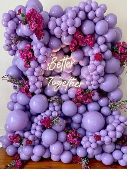 This is a popular choice for modern engagements. I created a dense wall of purple balloons in various sizes, accented with fresh flowers and a bright 'Better Together' neon sign for a chic photo backdrop.