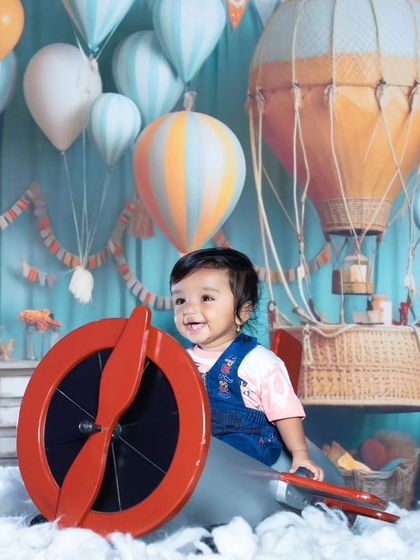 This little pilot is ready for takeoff in his propeller plane, surrounded by clouds and hot air balloons.