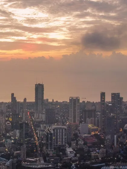 A closer view of the Mumbai skyline under a dramatic, cloud-filled sky at sunset.