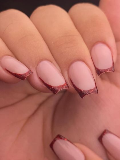 Simple, chic, and perfect for any occasion. This is a modern French manicure with a deep, curved tip using a beautiful red glitter polish on clean, square-shaped nails.