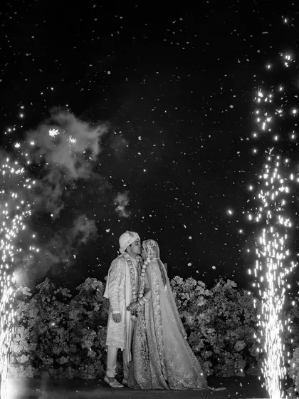 A surprising peck on the forehead after the varmala. This black and white shot captures the unexpected and sweet moment between the shy couple, Sugam and Anchit, under a sky of fireworks.