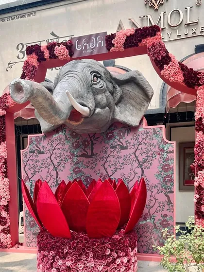 A majestic entrance created for luxury brand Anmol Jewellers. A large, sculpted elephant head emerges from a custom backdrop, framed by an arch of pink and crimson florals, making a powerful and artistic statement for the brand's event.