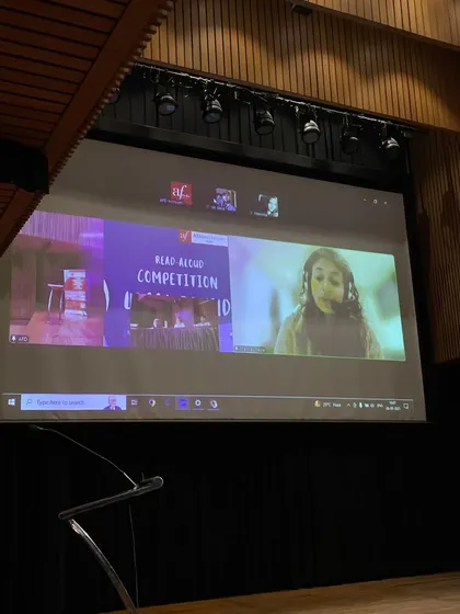A view of the Read-Aloud competition, with a participant joining virtually on the big screen. We embrace hybrid formats to make our events accessible to everyone.